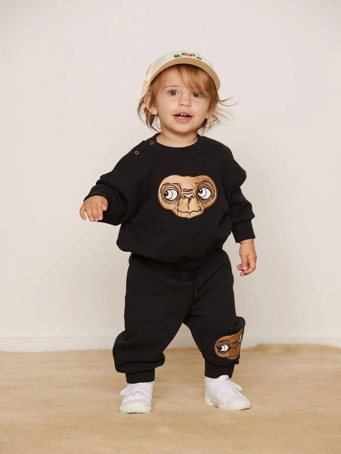 Niño con sudadera  negra con dibujo de E.T. y pantalones negros, ambas prendas de Mini Rodini.