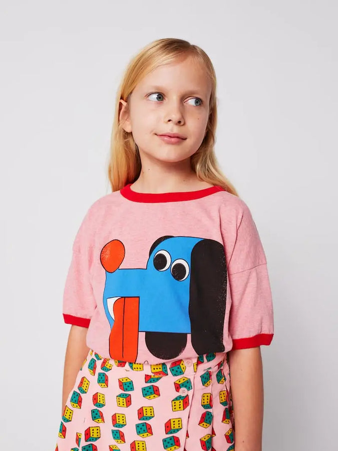 Niña con camiseta Doggy Mate y falda rosa de pana con estampado de dados, Bobo Choses aw25 moda infantil sostenible.