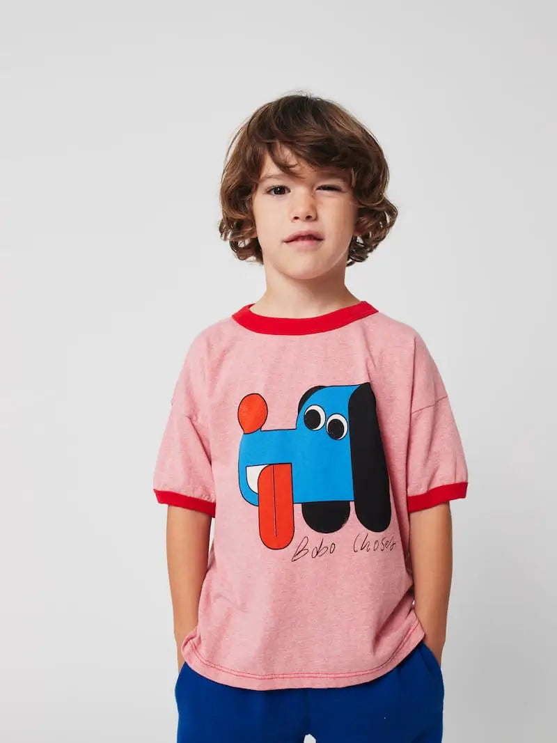 Niño con camiseta rosa de Bobo Choses  con dibujo de perrito y pantalón de color azul índigo. 
