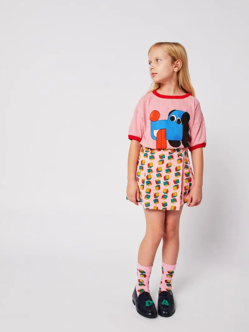 Niña con camiseta rosa de Bobo Choses con dibujo de perrito, y con falda corta de dados y calcetines a juego. 