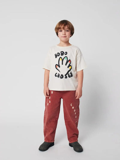 Niño vistiendo camiseta blanca y pantalones marrones de Bobo Choses.