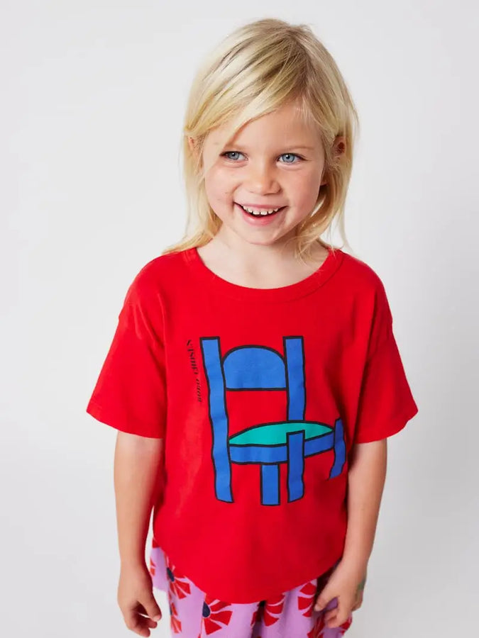 Niña vistiendo camiseta roja de manga corta de un dibujo de silla azul de Bobo Choses.