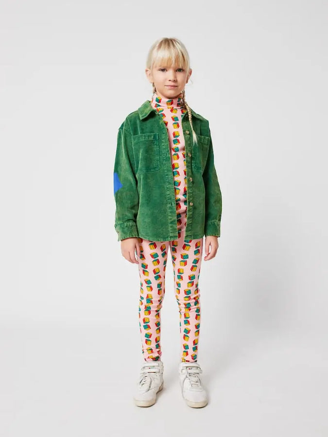 Niña vistiendo mallas de dados multicolores, camiseta de cuello alto con estampado de dados y camisa verde, todo de Bobo Choses.
