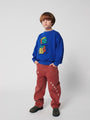 Niño vistiendo sudadera azul con dibujo de dados y pantalones marrones de Bobo Choses.