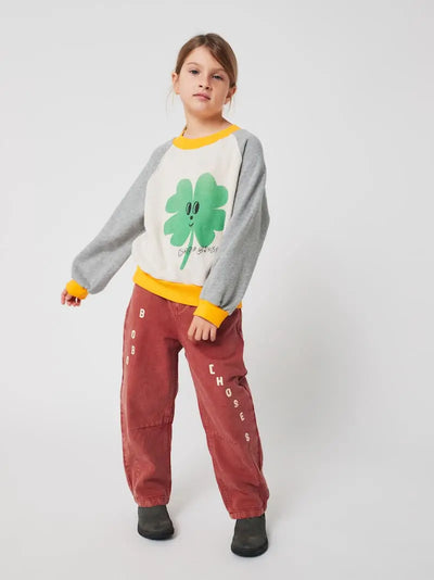 Niña vistiendo sudadera con dibujo de trébol y pantalones marrones de Bobo Choses.