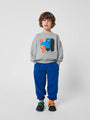 Niño con sudadera gris Doggy Mate y pantalones azules de Bobo Choses.