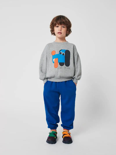 Niño con sudadera gris con dibujo de perro y pantalones azules de Bobo Choses.