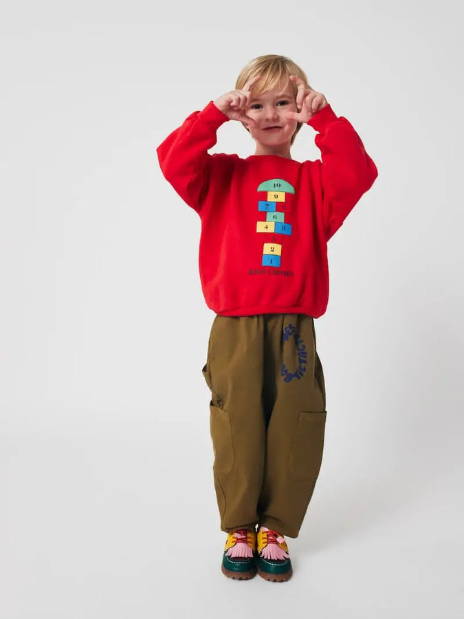 Niño con sudadera roja con dibujo de rayuela  multicoclor para niños y niñas de Bobo Choses.