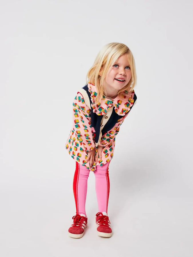 Niña con vestido rosa de dados multicolor, leotardos color block y chaleco azul con dibujo de caleidoscopio, todo de Bobo Choses.