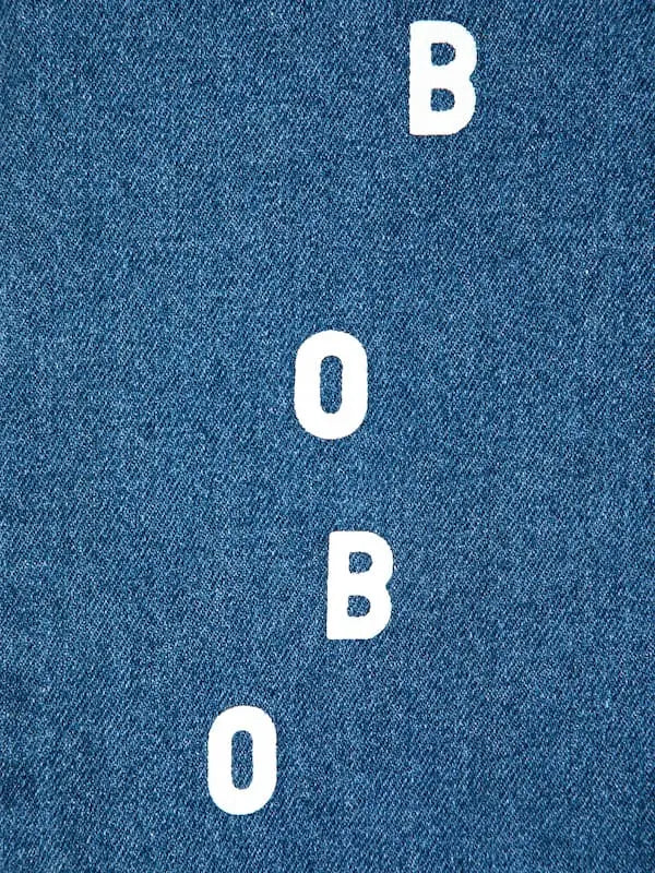 Detalle del logo de "Bobo" en la parte delantera de la pernera derecha, en los pantalones vaqueros azules. 