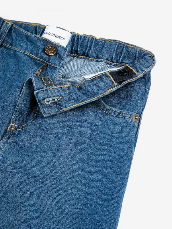 Detalle de cintura, botón y cremallera de los pantalones vaqueros azules con logo en la parte delantera. 