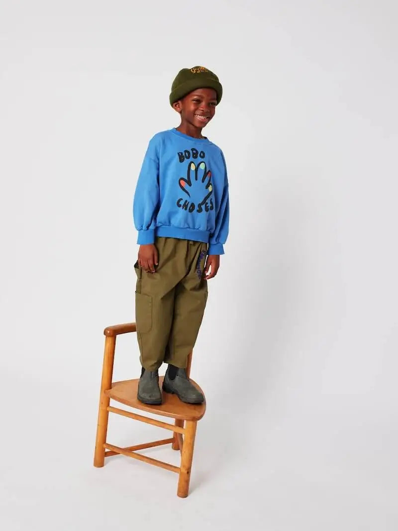 Niño vistiendo sudadera azul y pantalones  verdes de Bobo Choses.