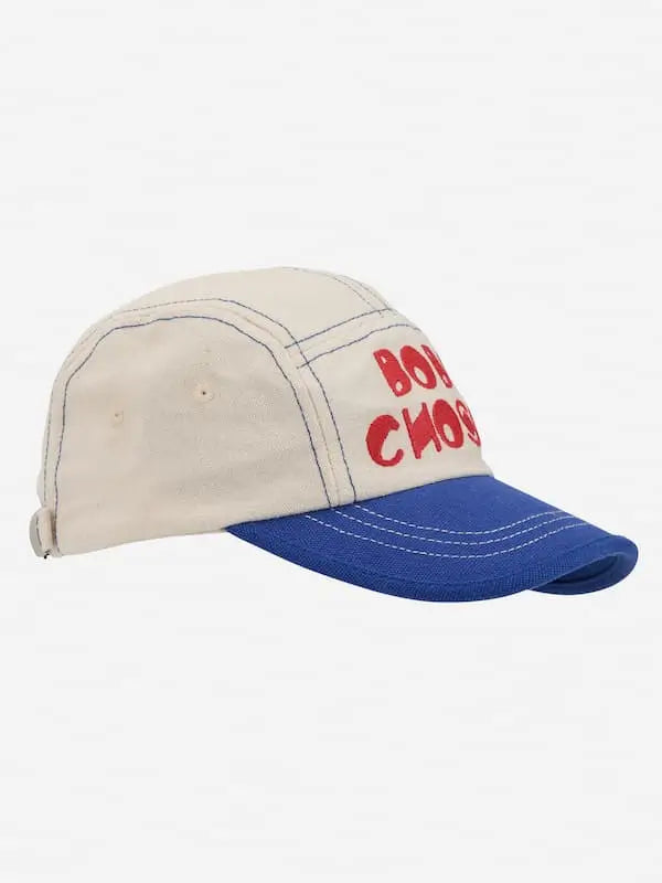 Vista de lado de la gorra color block blanca y morada con logo de Bobo Choses en rojo.