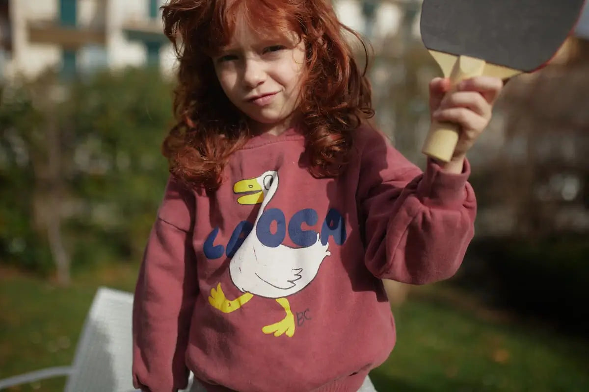 Niña vistiendo sudadera de color burdeos lavado con dibujo de oca en la parte delantera de Bobo Choses.