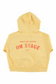 Vista atrás de la sudadera amarilla claro con capucha de Piupiuchick. Tiene texto On stage en la espalda.
