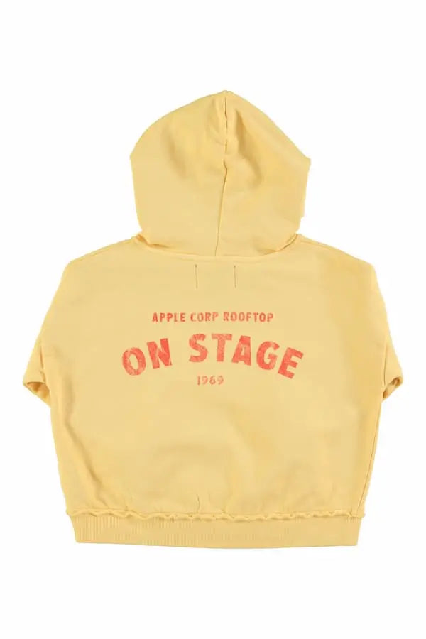 Vista atrás de la sudadera amarilla claro con capucha de Piupiuchick. Tiene texto On stage en la espalda.