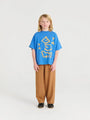 Niño vistiendo camiseta azul con dibujos de pájaros y pantalones marrones, ambas prendas de Weekend House Kids.