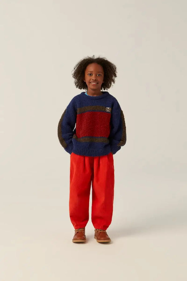 Niña con pantalones infantiles de pana roja The Campamento y jersey azul con bloque rojo en la parte delantera.