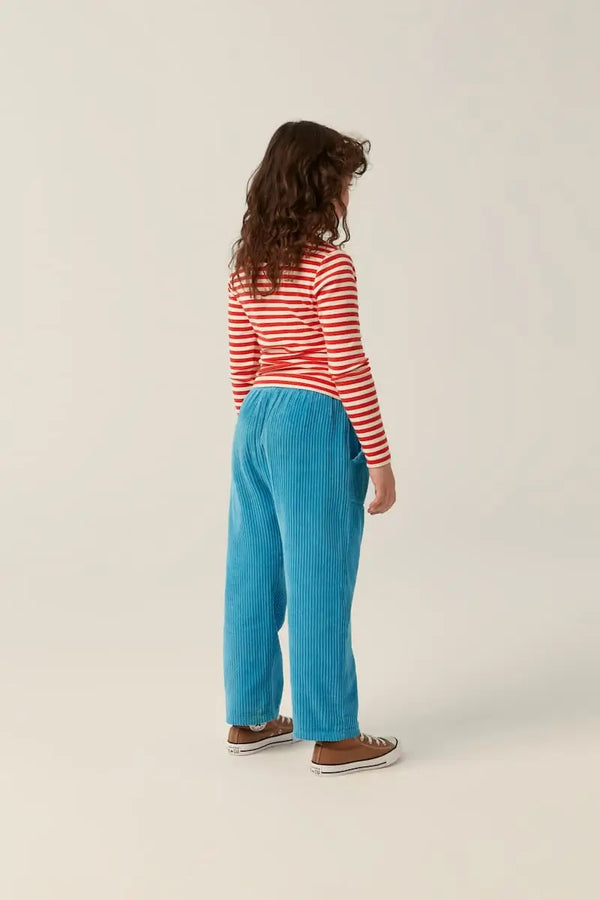 Niña con pantalón azul de pana y camiseta de cuello alto y manga larga de rayas blancas y rojas para niñas y niños de The Campamento.