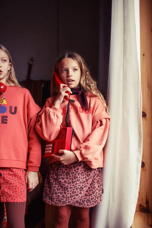 Niña con falda rosa de pana con estampado de animal print y sudadera rosa con texto "Hey Jude" de Piupiuchick.
