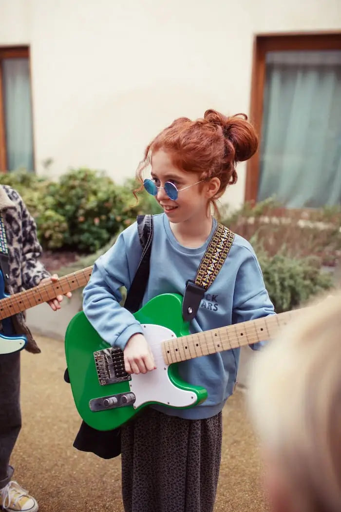 Niña con guitarra en la mano vestida de falda gris con animal print y sudadera azul "Rock stars" de Piupiuchick.