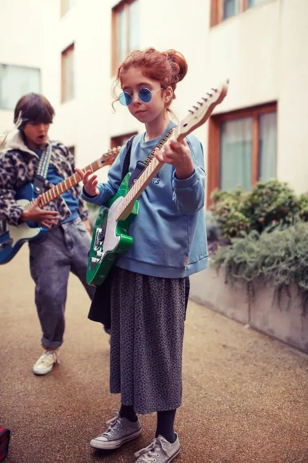 Niña con falda gris con animal print y sudadera azul con texto "rock stars" de Piupiuchick -vista trasera.