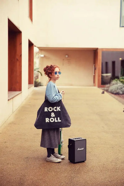 Niña con falda larga gris, sudadera azul y bolsa XL negra con texto "Rock & roll", todo de Piupiuchick.