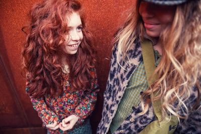 Dos niñas con ropa de la colección Piupiuchick otoño/invierno; una lleva blusa floral multicolor y la otra camisa de cuadros con abrigo estampado animal print.
