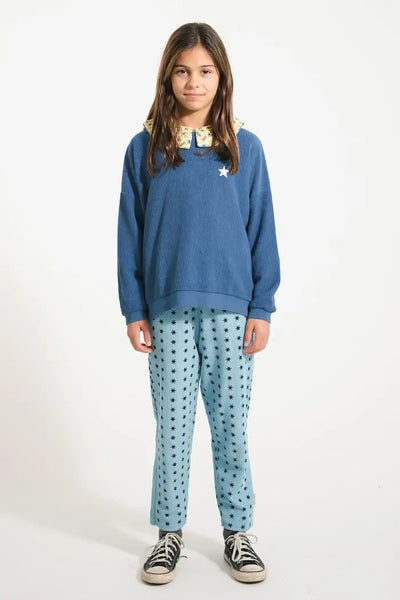 Niña con pantalones jogging azules con estampado de estrellas negras y sudadera  azul con estrella blanca en el pecho, Piupiuchick.