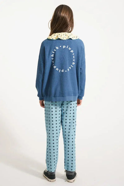 Vista trasera de niña con pantalones jogging azules con estampado de estrellas y sudadera azul con logo grande en la espalda de Piupiuchick.