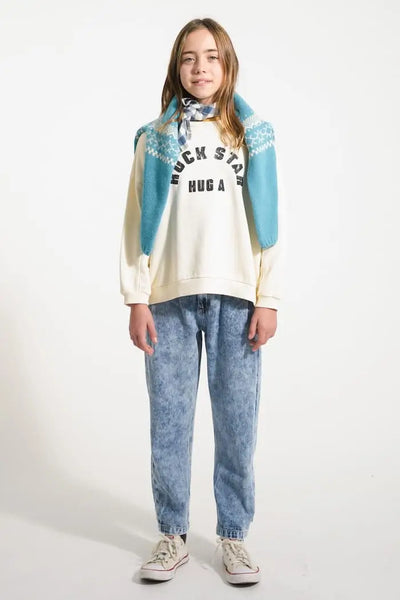 Niña con vaqueros azules mom fit y sudadera "Hug a Rock Star" en color crudo de Piupiuchick.