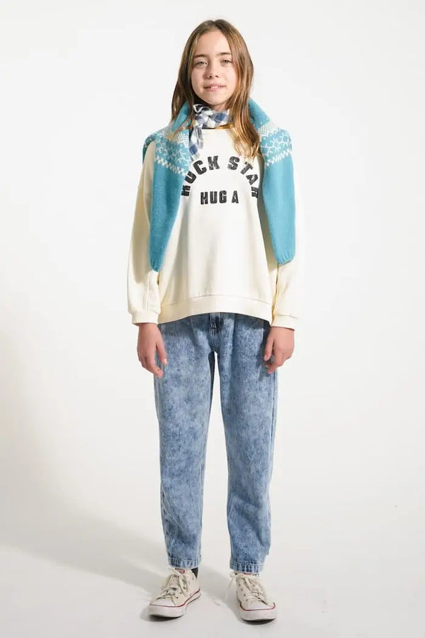 Niña con vaqueros azules mom fit y sudadera "Hug a Rock Star" en color crudo de Piupiuchick.