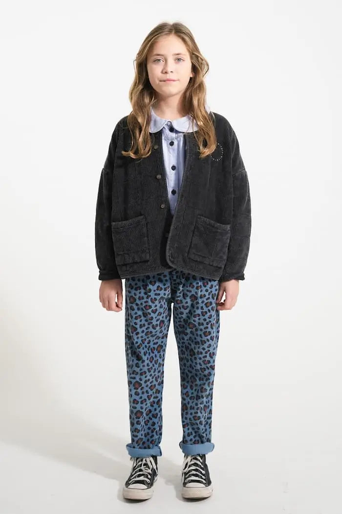 Niña vistiendo pantalones de pana con estampado animal print, blusa vaquera con cuello Peter Pan y chaqueta negra acolchada, todo de Piupiuchick.
