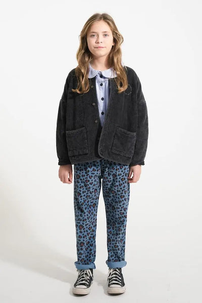 Niña vistiendo pantalones de pana con estampado animal print, blusa vaquera con cuello Peter Pan y chaqueta negra acolchada, todo de Piupiuchick.