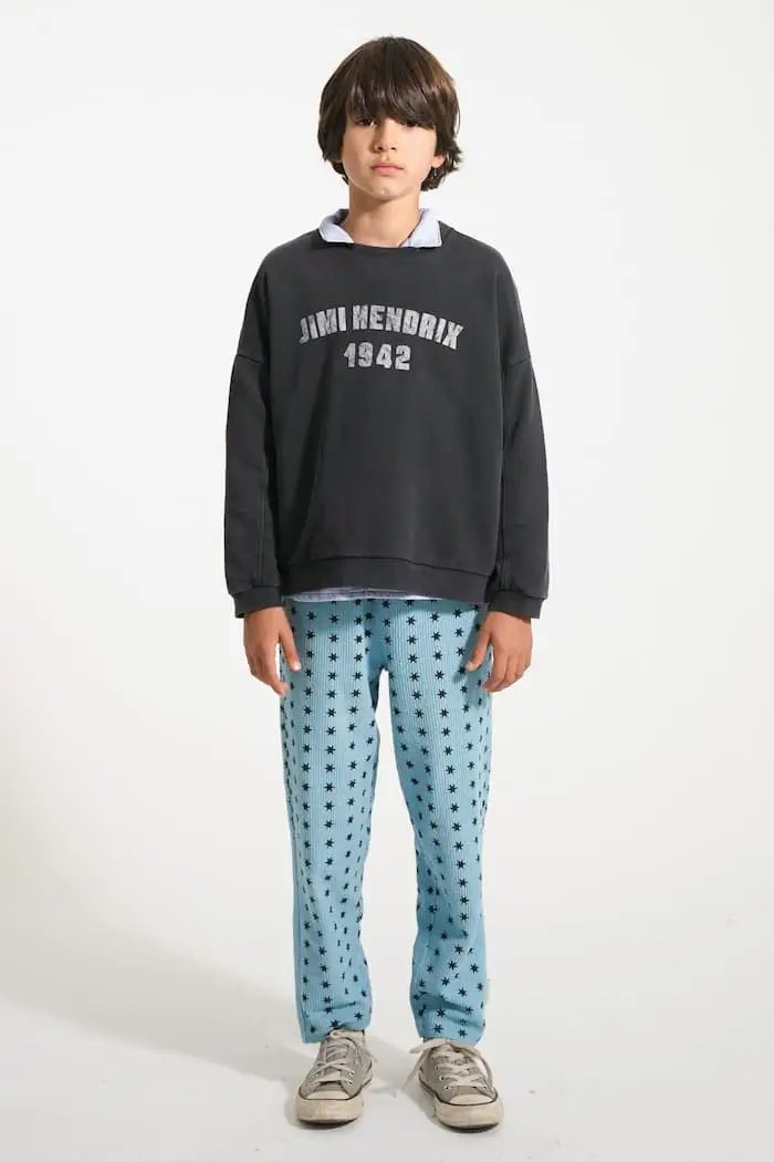 Niño con pantalones jogging azules con estrellas negras y sudadera negra "Jimi Hendrix 1942", vista delantera.