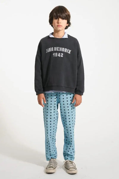 Niño con pantalones jogging azules con estrellas negras y sudadera negra "Jimi Hendrix 1942", vista delantera.