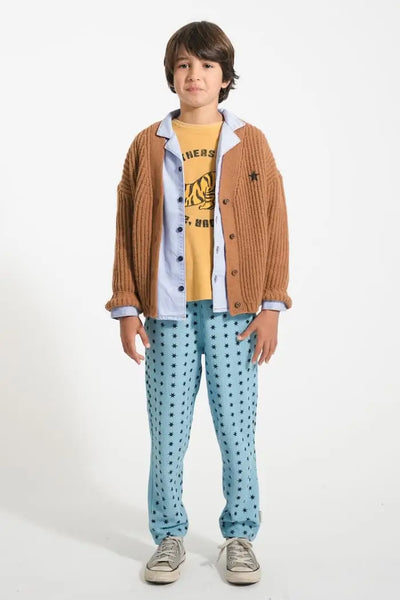 Niño con pantalones azules jogging con estampado de estrellas negras, camiseta mostaza de rizo y cárdigan marrón, todo de Piupiuchick.
