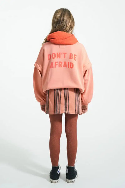 Niña con falda mini de rayas y sudadera rosa con texto "Don´t be afraid" , vista trasera, Piupiuchick.