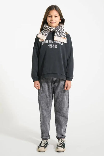 Niña con vaqueros negros mom fit, sudadera negra y bufanda rosa con animal print, todo de Piupiuchick.