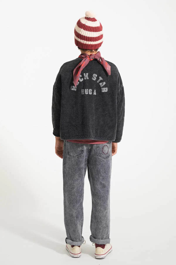 Niño con vaqueros negro, chaqueta negra y gorro de rayas de color burdeos y crudo de Piupiuchick otoño invierno 2025