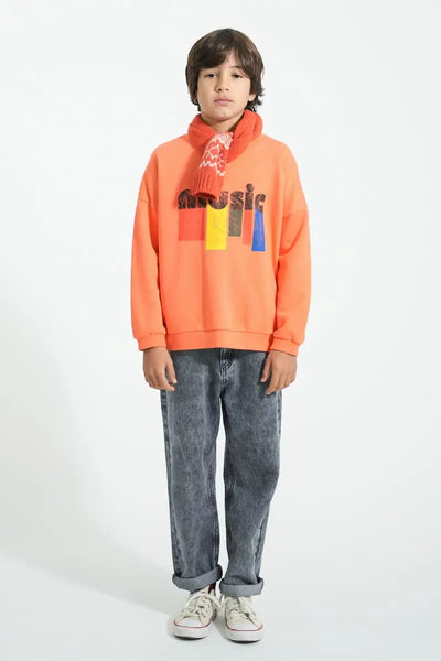 Niño con vaqueros negros unisex, sudadera naranja con texto Music y bufanda roja jaqcuard, todo de Piupiuchick.
