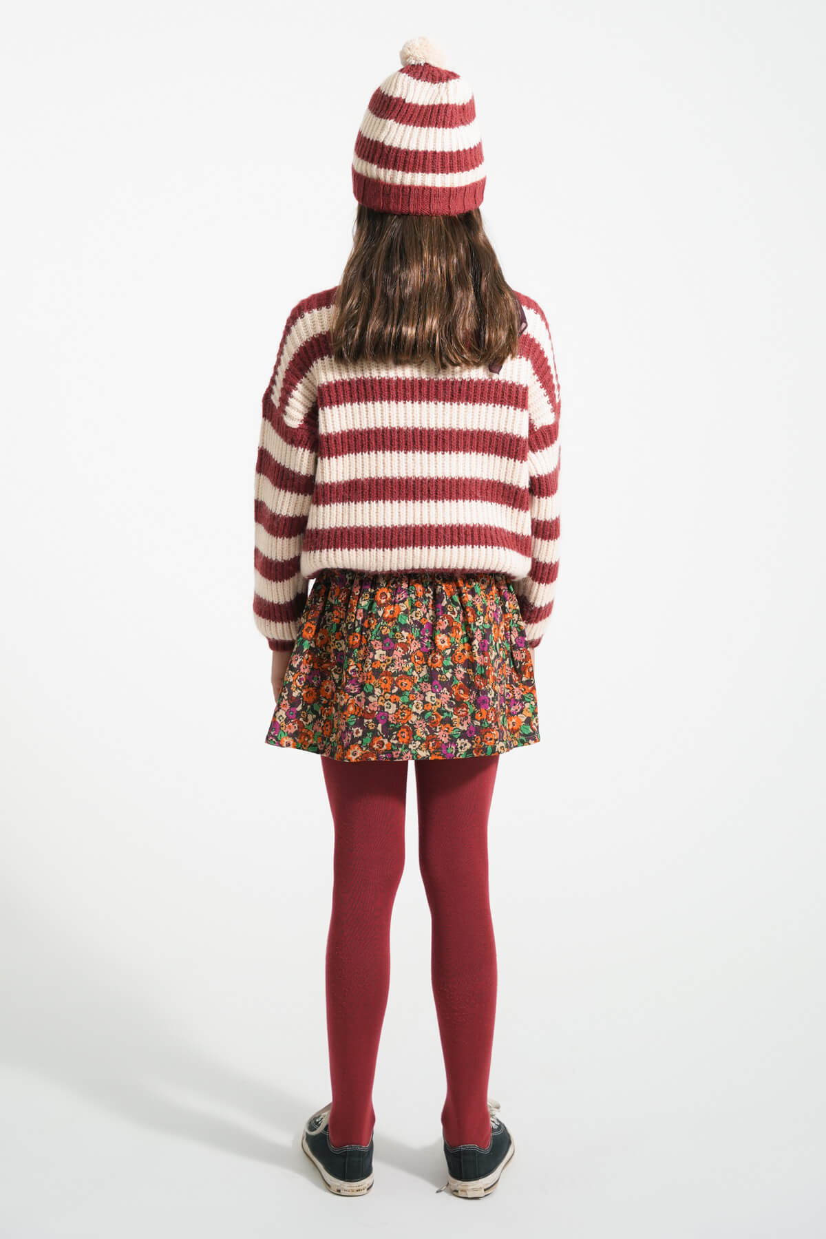 Niña vista atras con falda corta multicolor de flores, gorro de rayas y jersey de rayas de Piupiuchick