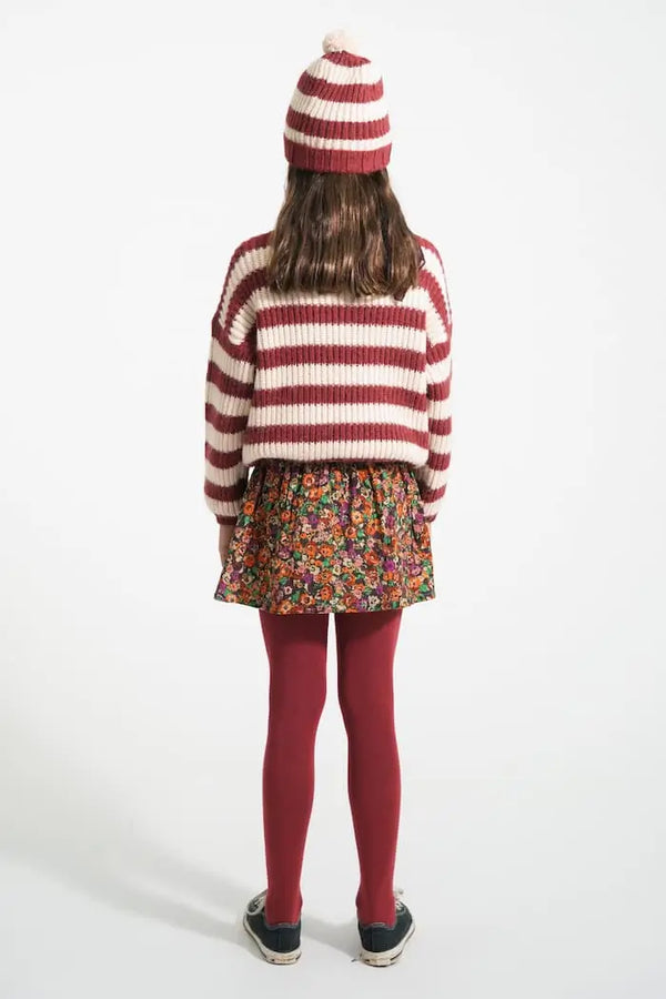 Vista atrás de una niña con falda corta de flores, jersey de rayas y gorro burdeos y crudo de Piupiuchick.