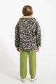 Niña con pantalones verdes de cuadros y chaqueta de animal print, vista atrás.
