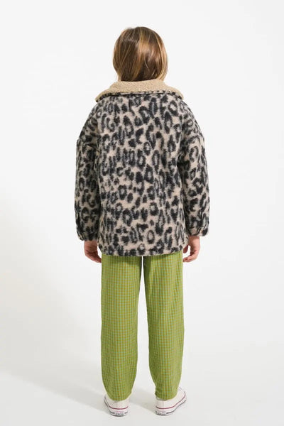 Niña con pantalones verdes de cuadros y chaqueta de animal print, vista atrás.
