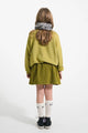 Vista atrás de niña con sudadera caqui y falda corta caqui con flores negros de Piupiuchick.