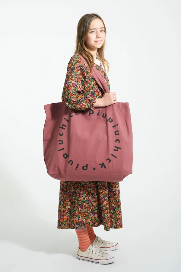 Niña con vestido largo de flores, bolsa XL burdeos de Piupiuchick y calcetines de rayas rosas y naranjas.