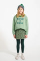 Niña con falda verde de animal print, sudadera verde con texto "Rock & Roll" y gorro gris con rayas verdes, todo de Piupiuchick.