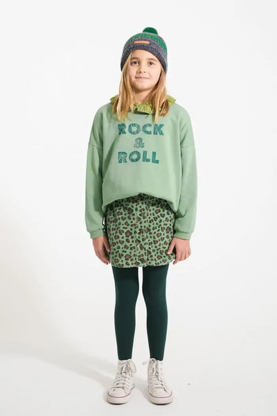 Niña con falda verde de animal print, sudadera verde con texto "Rock & Roll" y gorro gris con rayas verdes, todo de Piupiuchick.