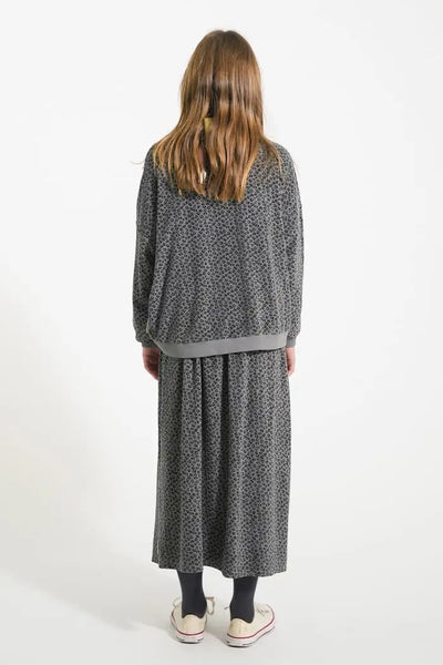 Niña con conjunto gris de rizo con estampado de animal print, falda larga y sudadera. Vista atrás, Piupiuchick.